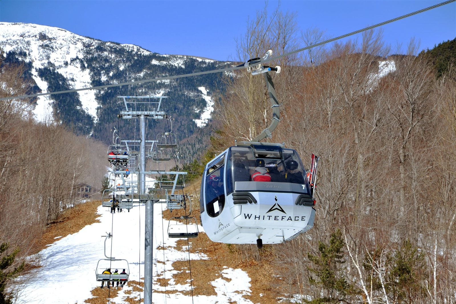 Gondola cabin rising over a groomed ski trail with a snow-covered summit behind